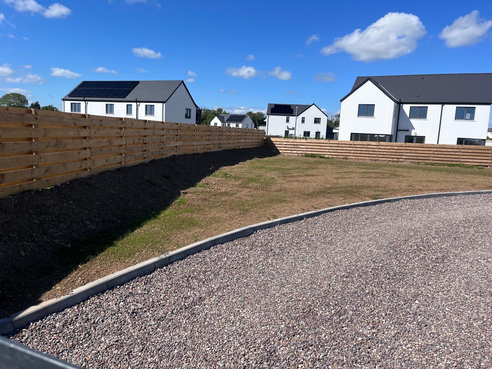 Established green lawn behind a timber sleeper retaining wall with a sweeping gravel drive